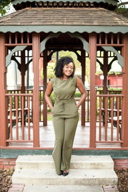 Woman in green jumpsuit standing in front of a wooden gazebo.